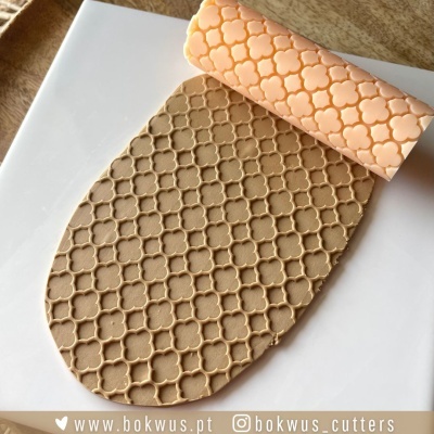 Rolo texturizador de silicone cor-de-rosa claro com padrão de arabescos e massa marrom clara texturizada.