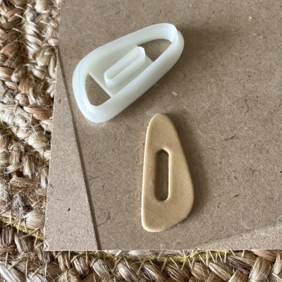 Dois botões triangulares, um branco de plástico e um bege de tecido, sobre cartão e tapete de fibras