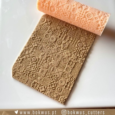 Rolo de cortador de massa com padrão geométrico e floral cor salmão e massa bege com textura correspondente.