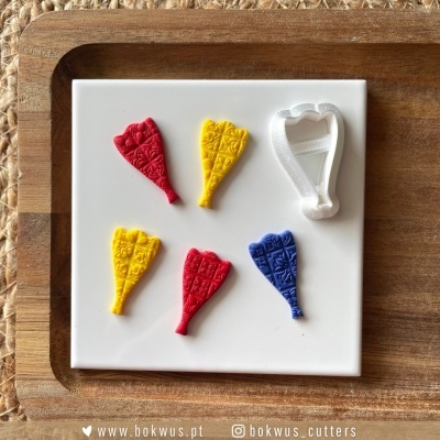 Formas decorativas em pasta flexível colorida com padrão geométrico e cortador branco sobre base branca e bandeja de madeira.