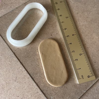 Molde oval branco, massa beige moldada e régua dourada sobre superfície bege