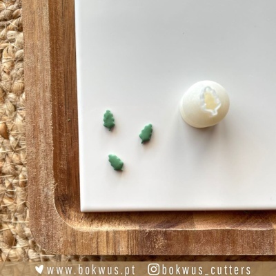 Três cortadores verdes em forma de folhas e carimbo branco sobre superfície branca com moldura de madeira