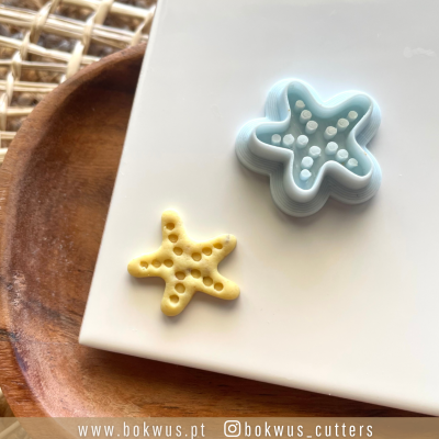 Cortadores de bolachas em forma de estrela-do-mar azul com bolacha amarela, sobre prato de madeira.