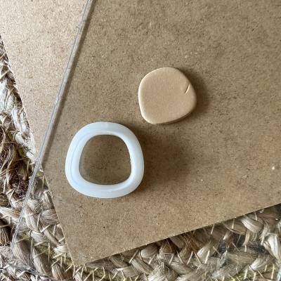 Duas peças pequenas, uma branca translúcida e uma castanha, sobre fundo castanho e tapete de fibras naturais.