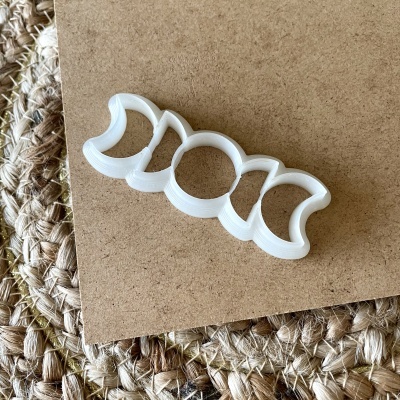 Cortador de bolachas em forma de fases da lua em plástico branco sobre madeira e tapete de juta