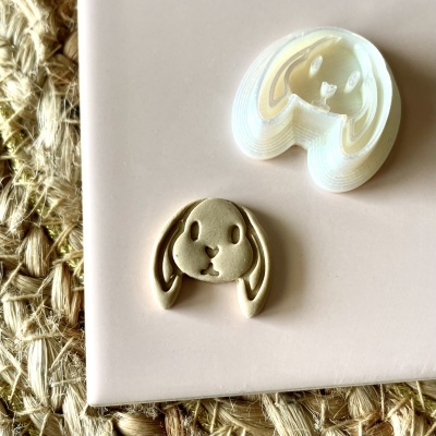 Cortador de biscoitos branco formato cabeça de coelho com biscoito bege ao lado sobre fundo rosa e tapete de fibras