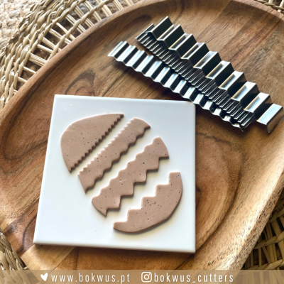 Cinco cortadores de massa de metal com design ondulado, massa moldada em formas semicirculares e tabuleiro de madeira.