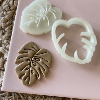 Três moldes para biscoitos em forma de folhas de cores branca e castanha sobre uma placa rosa e superfície texturizada.