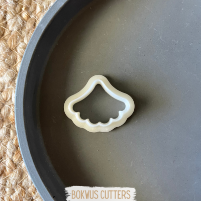 Cortante de biscoitos formato concha em plástico branco sobre prato cinzento