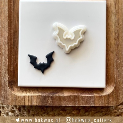 Dois cortadores de biscoito em forma de morcego branco e preto sobre azulejo branco com base de madeira