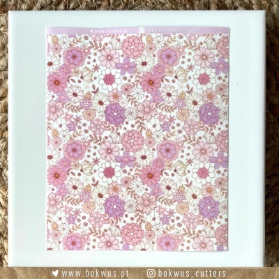 Quadrado de porcelana branca com estampa floral rosa fixada na madeira sobre tapete em ráfia