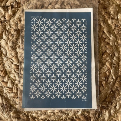 Cartão postal azul com padrão floral branco sobre tapete de fibras naturais