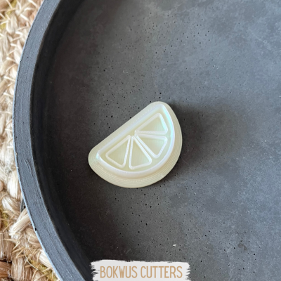 Cortador de massa em forma de limão branco sobre superfície preta redonda e tapete tecido.