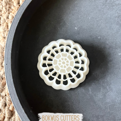 Cortante circular para pastelaria floral branco num prato preto sobre passadeira de fibras