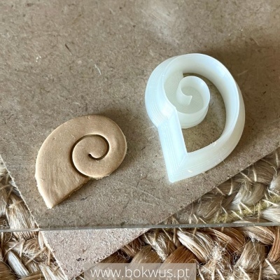 Dois objetos em espiral de cor bege e branco sobre superfície rústica com etiqueta www.bokwus.pt