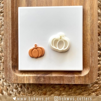 Dois cortadores de bolachas em forma de abóbora sobre azulejo branco e tábua de madeira