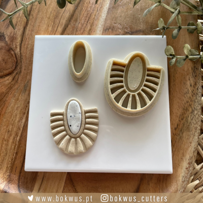 Três moldes bege e branco com padrões em oval e linhas, sobre base branca e madeira clara com ramos secos