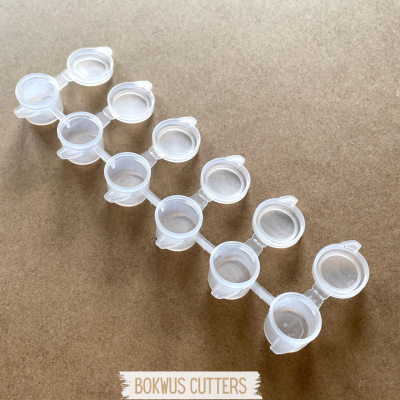 Recipientes plásticos pequenos ligados com tampas abertas sobre superfície castanha