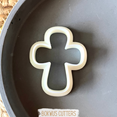 Cortador de biscoitos em forma de cruz branco numa superfície cinza fosco.