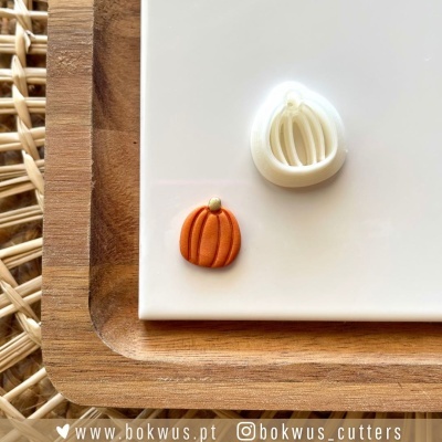 Dois cortadores de galletas em forma de abóbora sobre um prato branco com borda de madeira