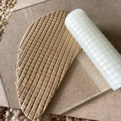 Rolo texturizador branco a criar padrão quadriculado em massa castanha