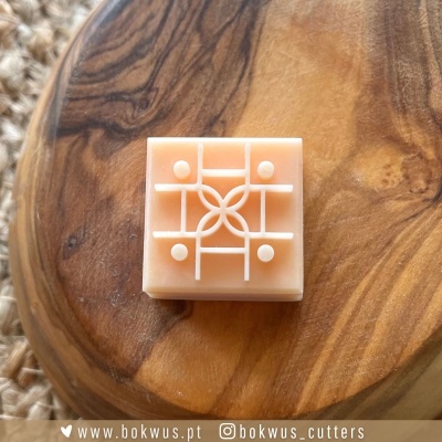 Cortador de bolachas quadrado cor pêssego claro com padrão branco em relevo sobre madeira