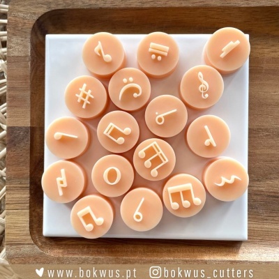 Biscoitos ou sabonetes com símbolos musicais brancos em relevo sobre placa branca e madeira