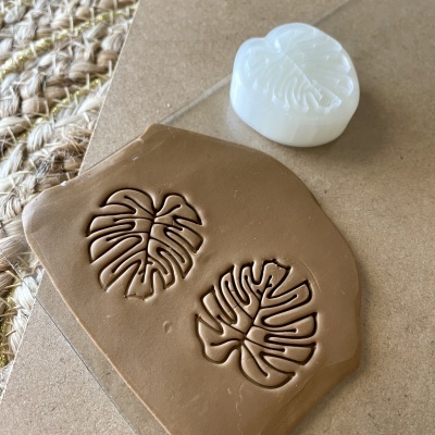 Selo de silicone branco com padrão de folha sobre argila castanha clara.