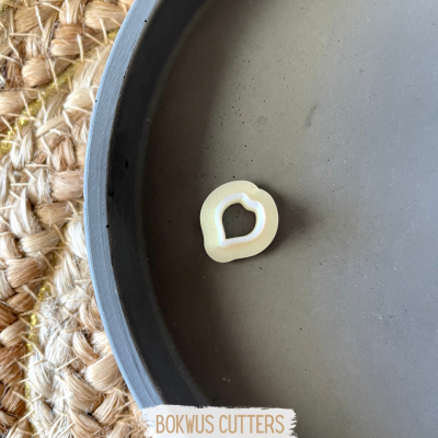 Cortador de bolachas pequeno de plástico branco em forma de melancia dentro de bandeja cinza sobre carpete trançado