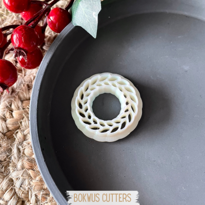 Cortante de massa redondo branco com padrão de folhas dentro de prato cinzento e decoração com bagas vermelhas