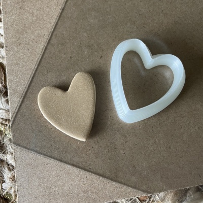 Coração de esponja bege e cortador de biscoitos branco em superfície castanha