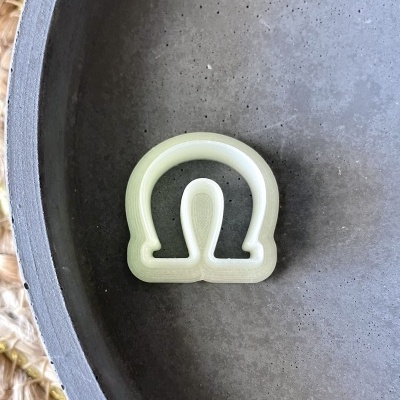 Cortador de biscoitos formato ômega em prato cinza sobre tapete de fibra