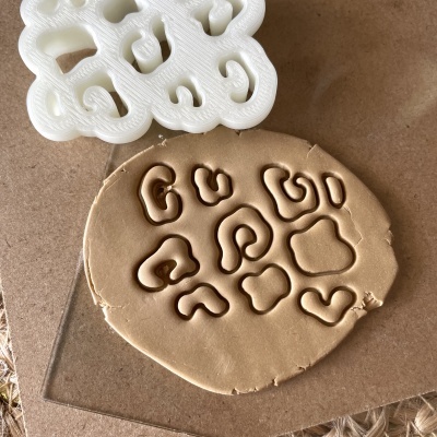 Cortador de biscoitos branco em forma de letras sobre massa castanha clara