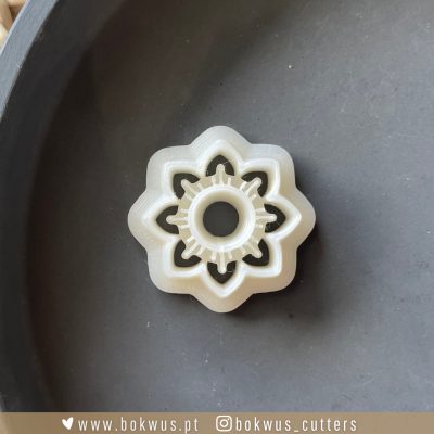 Cortador de biscoitos branco em forma de flor com recortes sobre superfície cinzenta