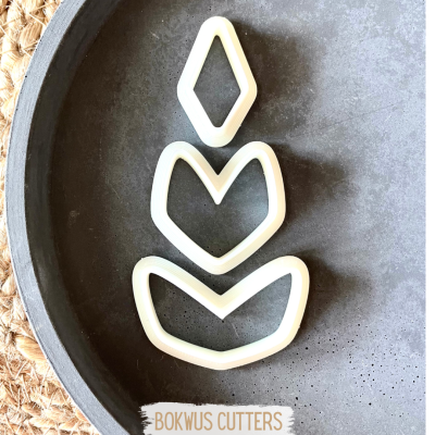 Três cortadores de massa brancos em forma de folhas numa tigela cinza