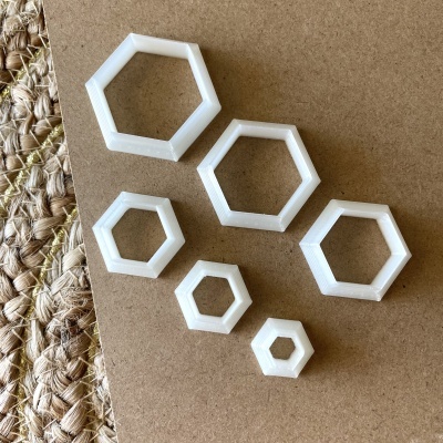 Anéis hexagonais brancos de plástico numa superfície castanha com textura trançada ao lado.