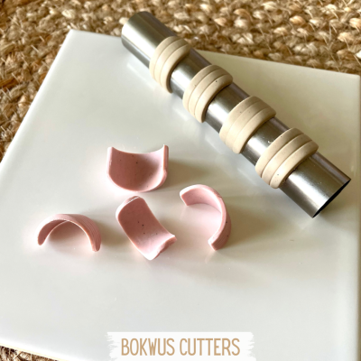 Anéis de silicone bege no tubo metálico com cortantes rosa em base branca com fundo de corda