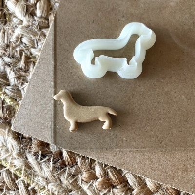 Cortador de bolachas branco e bolacha castanha em forma de cão dachshund sobre cartão e tapete de fibras naturais