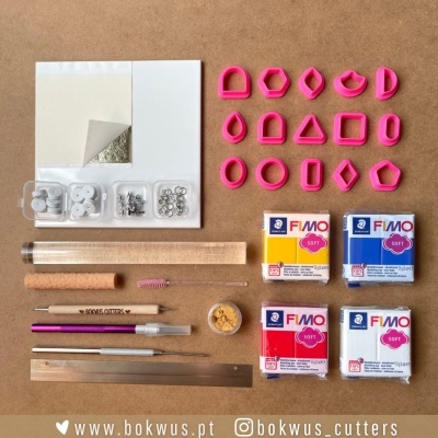 Kit de ferramentas e argila FIMO Soft com cortadores geométricos rosa e acessórios de modelagem sobre mesa castanha.