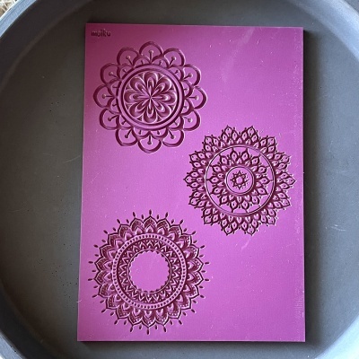 Molde de silicone rosa com padrões florais decorativos em relevo dentro de forma metálica redonda