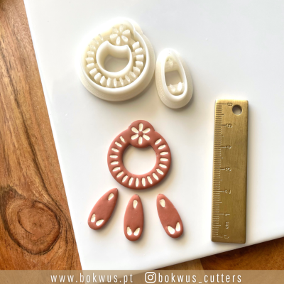 Conjunto de cortadores de massa em plástico branco com régua dourada ao lado, sobre superfície branca e madeira.