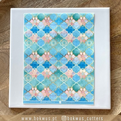 Azulejo branco com padrão colorido azul, verde e rosa com texto na base sobre madeira