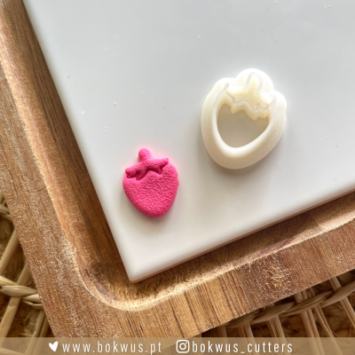 Cortador de biscoitos branco em forma de morango com peça rosa de massa modelada sobre bandeja de madeira