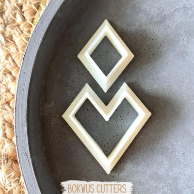 Cortadores de massa brancos em formas geométricas sobre prato preto e base de palha