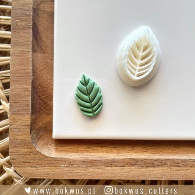 Cortador de massa em forma de folha com massa verde recortada, sobre prato branco e base de madeira