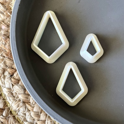 Três cortadores de massa losango brancos em bandeja cinza junto a tapete de fibras naturais