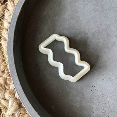 Cortador branco ondulado sobre superfície cinzenta com tapete de fibra natural ao lado