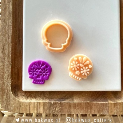 Três cortantes para bolachas em forma de caveira sobre base branca com estrutura de madeira.