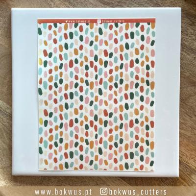 Cartão colorido com padrão de manchas verticais sobre placa branca e madeira