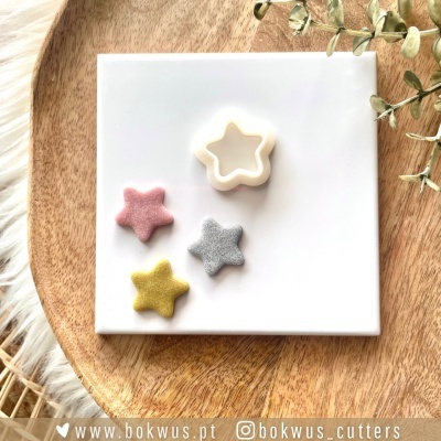 Cortador de biscoitos em forma de estrela branco e três biscoitos coloridos em forma de estrela sobre uma placa branca e um tabuleiro de madeira